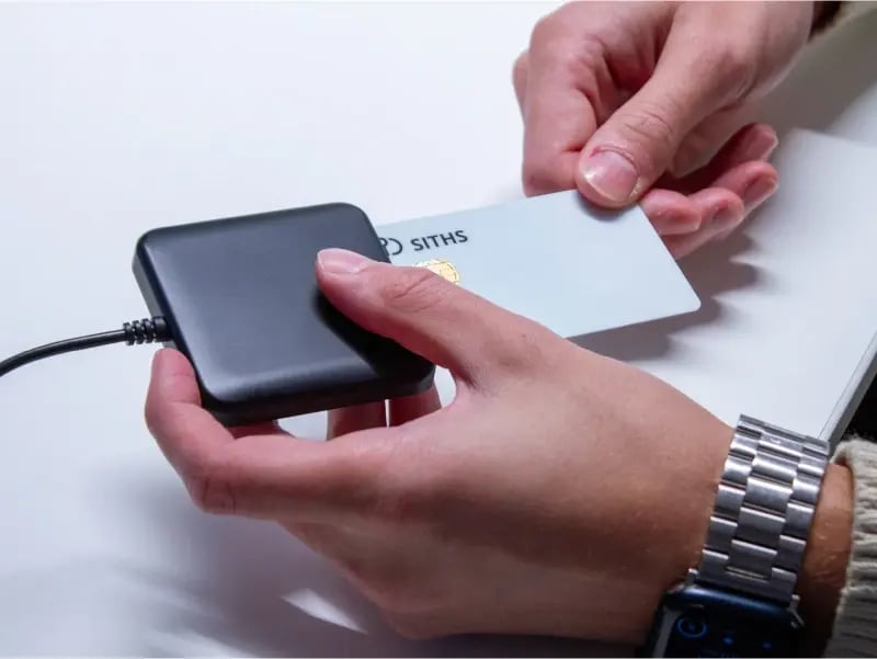 Två händer som visar hur ett SITHS-kort placeras i en kortläsare.