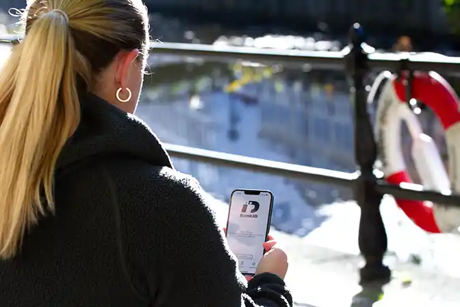 Fotografi- en kvinna genomför en BankID-inloggning via mobil en solig höstdag