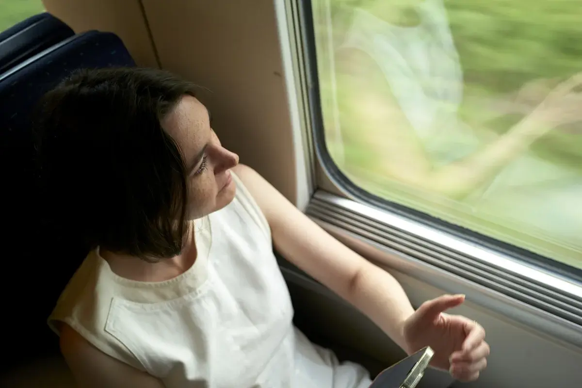 bild på en tjej som sitter och tittar ut från ett tåg och håller en mobil i handen